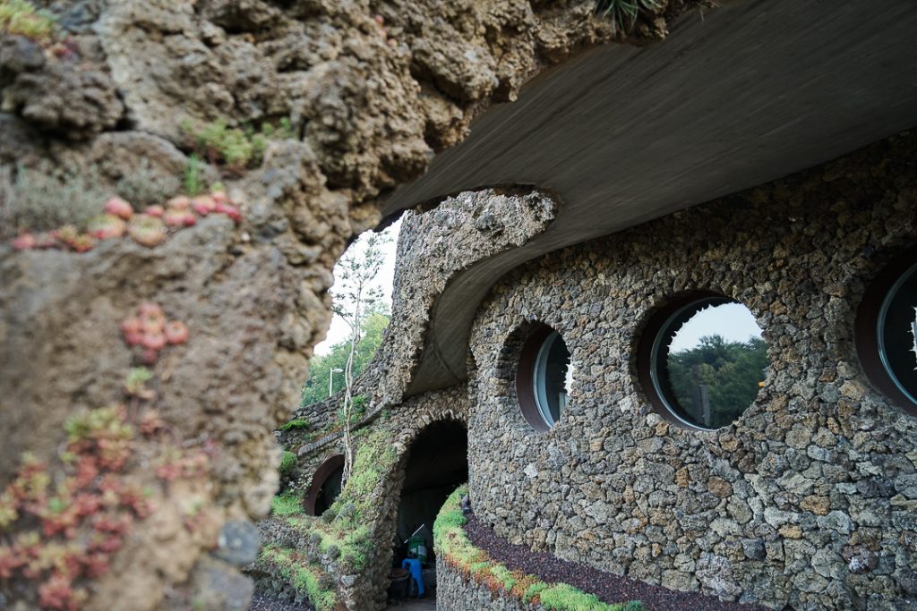 Fachada de piedra de La Casa Verda con ventanas circulares, muros curvos y vegetación.